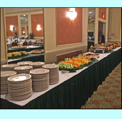 photos shows a long table with piles of plates colorful vegetables and 4 or 5 large steam tables.
