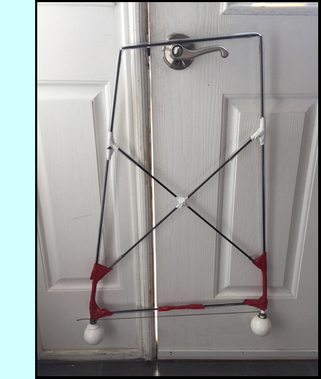 photo shows a rectangular frame hanging on a doorknob. The vertical sides of the frame are canes with white tips, and are connected to each other with two bars crossing each other.