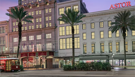picture of Astor hotel, close to street with palm trees along the sidewalk and a streetcar in front.