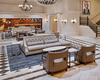 Large lobby of hotel with several large couches and armchairs, coffee tables and a stairway with a golden railing.